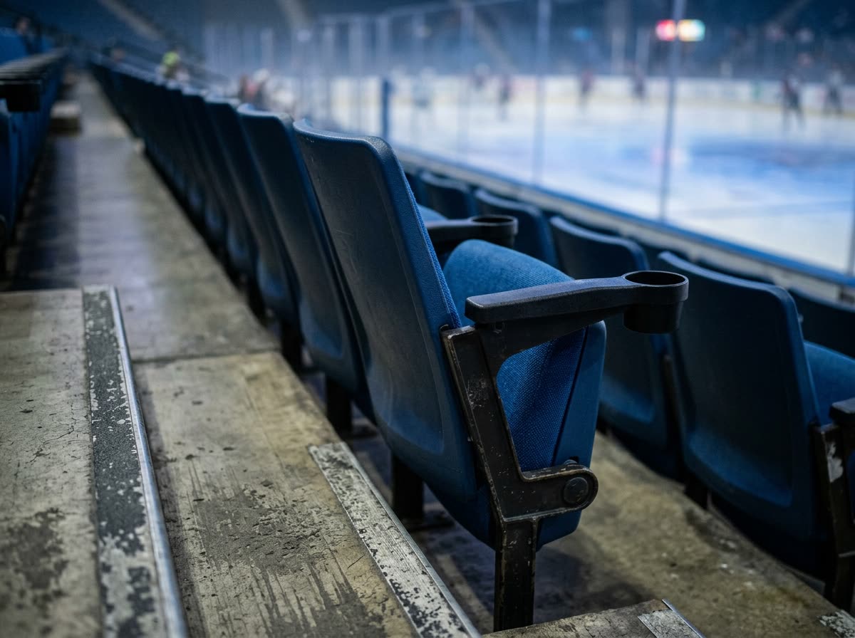 Close-up of a row of empty arena seats with armrests and cupholders in low light.